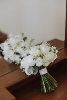 Wedding bouquet. White cut roses, green seed heads and leaves. Green stems and white ribbon and gold wedding rings. photo