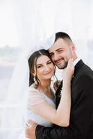 un hermoso novio abraza su novia en un lozano blanco vestir y sonrisas en un hermosa al aire libre ajuste. debajo el abierto cielo. alto calidad foto. un recién casado Pareja poses juntos en un soleado verano día. foto