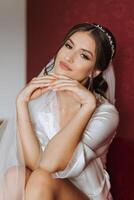 Beautiful bride in a dressing gown in the morning before the wedding ceremony. Incredible hairstyle of the bride. Natural and modern makeup. Portrait of a young bride in a dressing gown. photo