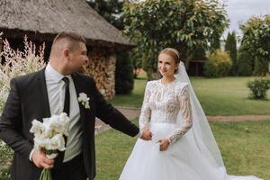 A handsome groom and an elegant bride in a lush white dress are walking in a summer park. Happy bride and groom getting ready for their best day. photo