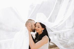 Close-up portrait of two people in love. An affectionate groom embraces the bride, supporting her under the veil. The best moments of the wedding. photo