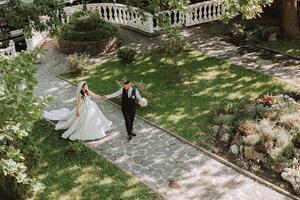A handsome groom and an elegant bride in a lush white dress are walking in a summer park. Happy bride and groom getting ready for their best day. photo