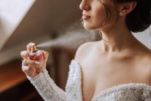 The brunette bride, holds perfume in her hands, wants to apply it on herself. Voluminous veil. Beautiful hands. Open bust photo