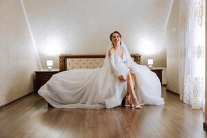 Young brunette in long wedding dress and veil in hotel room. A charming bride, full length, in a magnificent white dress on the morning before the wedding. photo