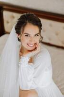 Beautiful bride in a dressing gown in the morning before the wedding ceremony. Incredible hairstyle of the bride. Natural and modern makeup. Portrait of a young bride in a dressing gown. photo