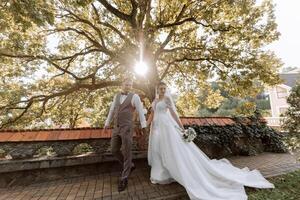 A handsome groom and an elegant bride in a lush white dress are walking in a summer park. Happy bride and groom getting ready for their best day. photo