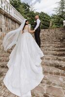 A handsome groom and an elegant bride in a lush white dress are walking in a summer park. Happy bride and groom getting ready for their best day. photo