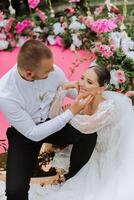 Beautiful couple sitting and hugging outdoors on their wedding day, relaxing on the best summer day. A handsome groom and an elegant bride in a magnificent wedding dress. photo