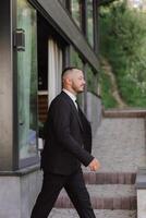 retrato de el novio en naturaleza en el verano. elegante alto novio en un elegante negro negocio traje. empresario en naturaleza. retrato de un exitoso hombre. Boda retrato de el novio. foto