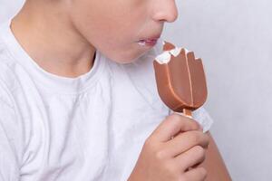 A boy whose face is unrecognizable eats ice cream covered in chocolate. photo