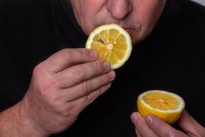 An unrecognizable man eats a sour lemon. photo