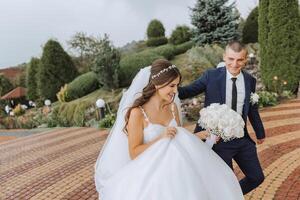 Stylish happy bride and groom running on the background of beautiful nature. Wedding. Beautiful emotional couple smiling and having fun in the rain in a European city. photo