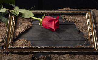 In a beautiful frame, pieces of canvas and a red rose on a wooden background. photo