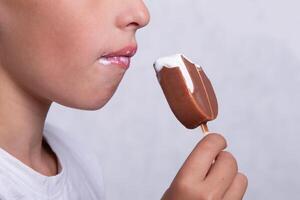 A boy whose face is unrecognizable eats ice cream covered in chocolate. photo