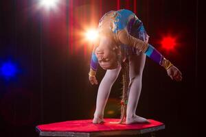 A girl with a flexible body. Performs a circus artist. Circus gymnast. Balancing act. The child performs an acrobatic trick photo