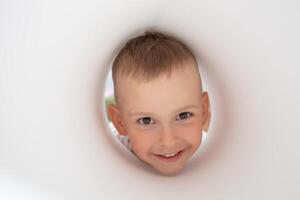 The face of a funny little boy looking into a paper hole. photo