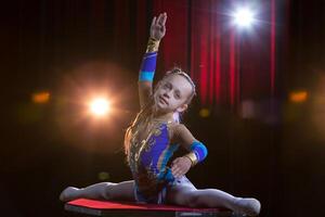 A girl with a flexible body. Performs a circus artist. Circus gymnast. Balancing act. The child performs an acrobatic trick photo