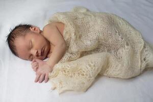 Newborn baby wrapped in a knitted blanket on a light background. photo
