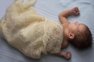 Newborn baby wrapped in a knitted blanket on a light background. photo