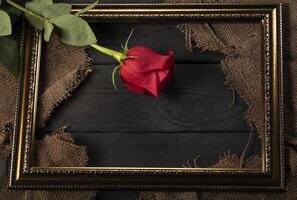 In a beautiful frame, pieces of canvas and a red rose on a wooden background. photo