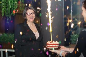 un de edad mediana mujer celebra su cumpleaños. un mujer se regocija, mira a un cumpleaños pastel con un ardiente vela. foto