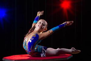 un niña con un flexible cuerpo. realiza un circo artista. circo gimnasta. equilibrio acto. el niño realiza un acrobático truco foto