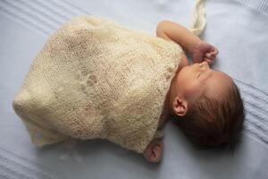 Newborn baby wrapped in a knitted blanket on a light background. photo