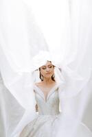 portrait of a beautiful young bride in a white dress with a long veil and a gorgeous hairstyle. Smiling bride. Wedding day. Gorgeous bride. Marriage. photo