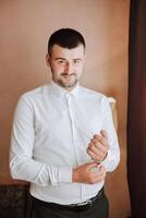 Business shirt. A man in a white shirt fastens the buttons. Young politician, male style, businessman buttoning shirt, male hands close-up, american, european businessman photo