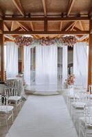 el blanco arco es decorado con rosado flores blanco alfombra y blanco sillas. preparación para el Boda ceremonia foto