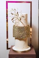 a three-tier wedding cake of golden color, decorated with flowers, stands on a decorative stand. Decorative wedding cake. Beauty is in the details. photo