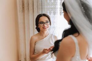 Wedding morning. Bridesmaids help put on the white wedding dress. A young woman is preparing to meet her groom and having fun with her friends photo