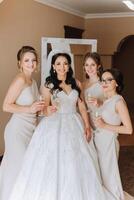 Photo bride with her friends drinking champagne from glasses. Cropped shot of a beautiful young bride and her bridesmaids having champagne before the wedding.