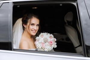 The bride looks out of the car window. Close-up portrait of a pretty shy bride in a car window. Bride smile emotions photo