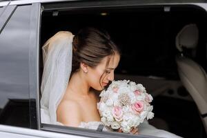 The bride looks out of the car window. Close-up portrait of a pretty shy bride in a car window. Bride smile emotions photo