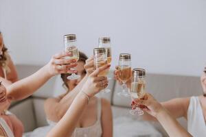 Photo bride with her friends drinking champagne from glasses. Cropped shot of a beautiful young bride and her bridesmaids having champagne before the wedding.