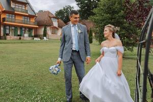 A handsome groom and an elegant bride in a lush white dress are walking in a summer park. Happy bride and groom getting ready for their best day. photo