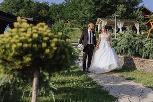A handsome groom and an elegant bride in a lush white dress are walking in a summer park. Happy bride and groom getting ready for their best day. photo