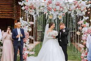 el novio llantos durante el Boda ceremonia cerca el flor arco. verano Boda en naturaleza. ella dijo Sí. un conmovedor momento a el Boda ceremonia foto