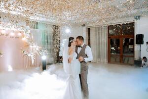 Wedding dance of the bride and groom. The first dance of the bride and groom in an elegant wedding hall with the use of heavy smoke and pyrotechnic lights, confetti. photo