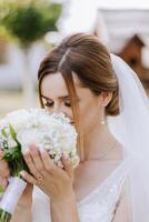 un encantador novia en un increíblemente hermosa vestir disfruta un ramo de flores y olfatea él. verano boda. un lujoso novia. foto