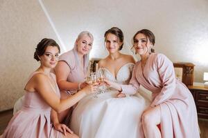 Photo bride with her friends drinking champagne from glasses. Cropped shot of a beautiful young bride and her bridesmaids having champagne before the wedding.