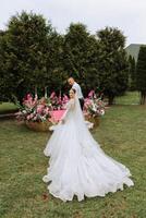 A handsome groom and an elegant bride in a lush white dress are walking in a summer park. Happy bride and groom getting ready for their best day. photo