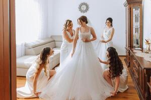 Wedding morning. Bridesmaids help put on the white wedding dress. A young woman is preparing to meet her groom and having fun with her friends photo