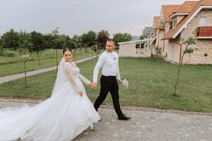 A handsome groom and an elegant bride in a lush white dress are walking in a summer park. Happy bride and groom getting ready for their best day. photo