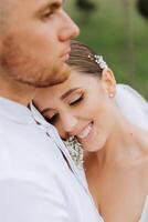A handsome groom embraces his bride in a lush white dress and smiles in a beautiful outdoor setting. Under the open sky. High quality photo. A newlywed couple poses together on a sunny summer day. photo