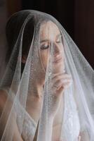 hermosa joven novia participación velo en blanco Boda vestido, retrato de morena novia en hotel habitación, Mañana antes de boda. foto