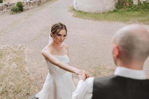 A handsome groom and an elegant bride in a lush white dress are walking in a summer park. Happy bride and groom getting ready for their best day. photo