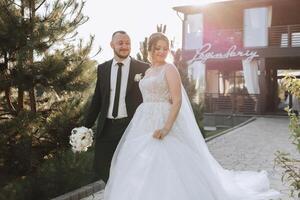 A handsome groom and an elegant bride in a lush white dress are walking in a summer park. Happy bride and groom getting ready for their best day. photo