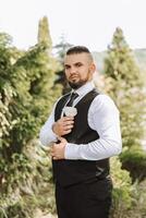 Portrait of the groom in nature in the summer. Stylish tall groom in an elegant black business suit. Businessman in nature. Portrait of a successful man. Wedding portrait of the groom. photo